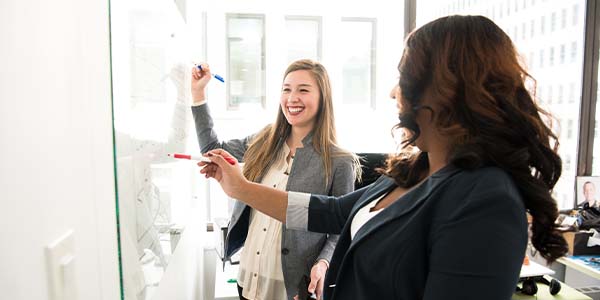 two business women writing on whiteboard