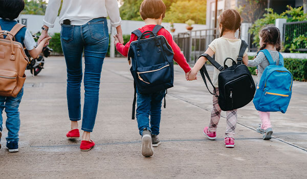 Adult and four children wearing backpacks walking hand in hand down a sidewalk