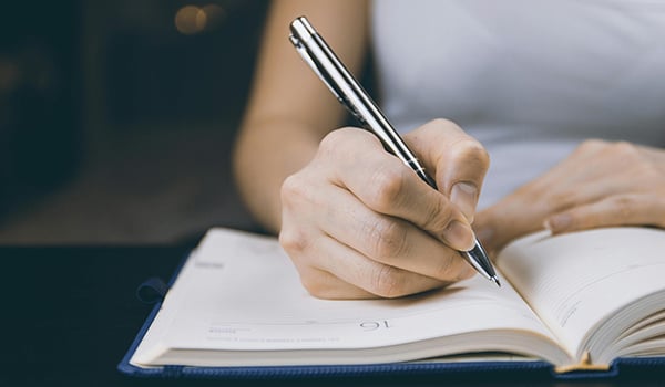 Close-up of a hand writing in an open journal with a silver pen