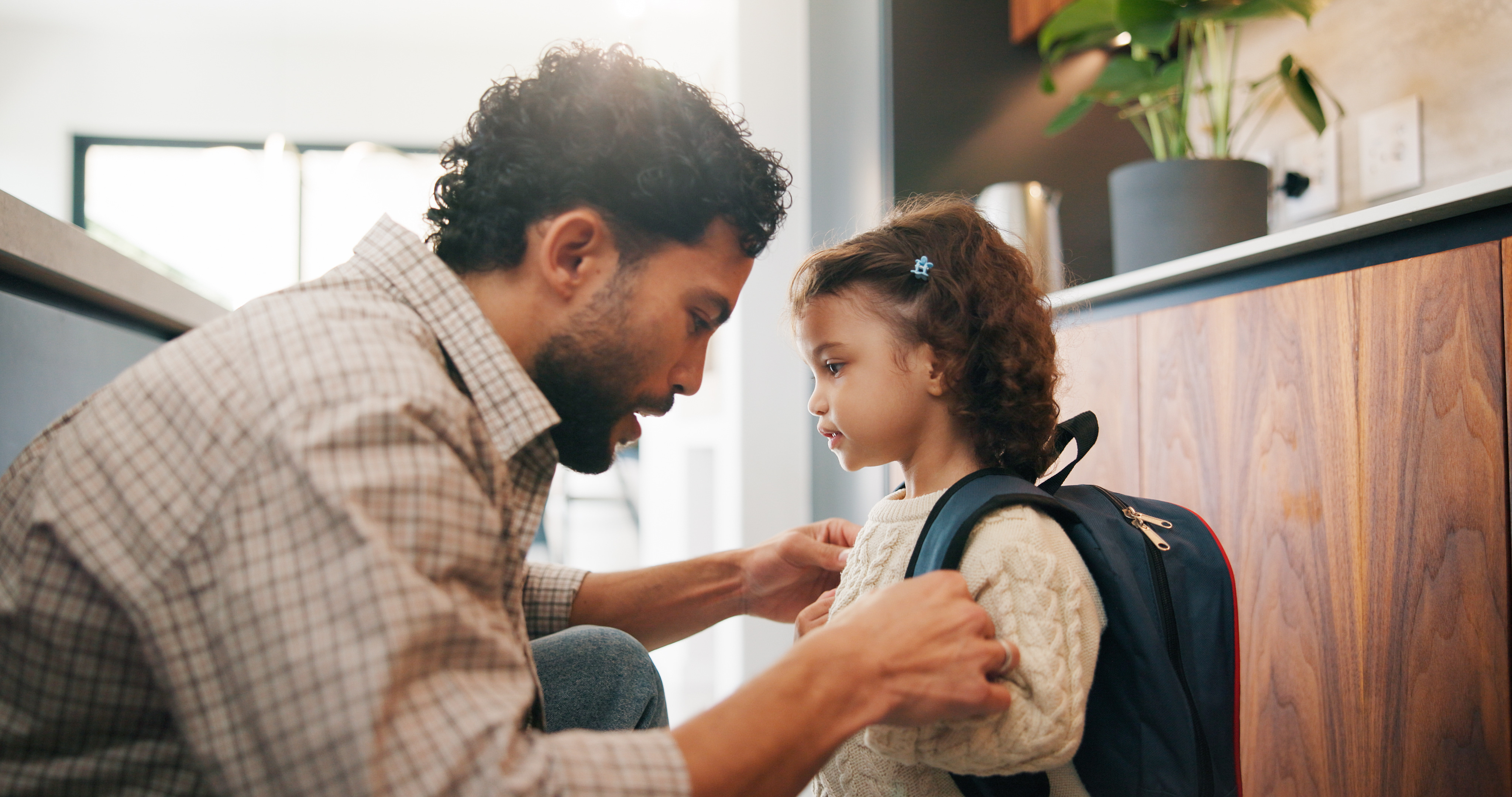 A father helping his young daughter get ready for school.