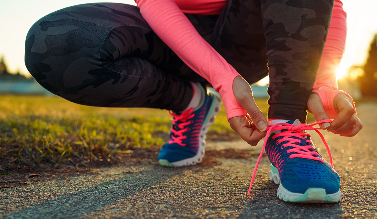 A runner tying up their sneakers with the sun setting in the back.