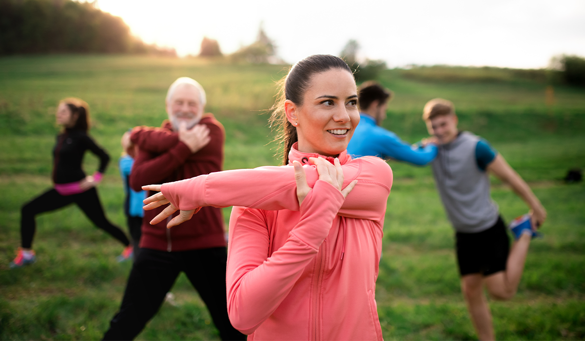 People participate in a group stretching activity outdoors on a grassy field.