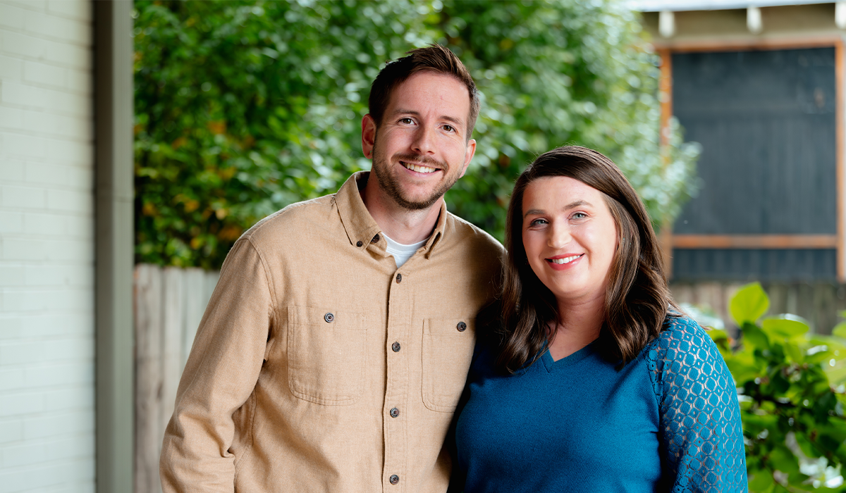 Jordan and Anna smile together with trees in the background. 
