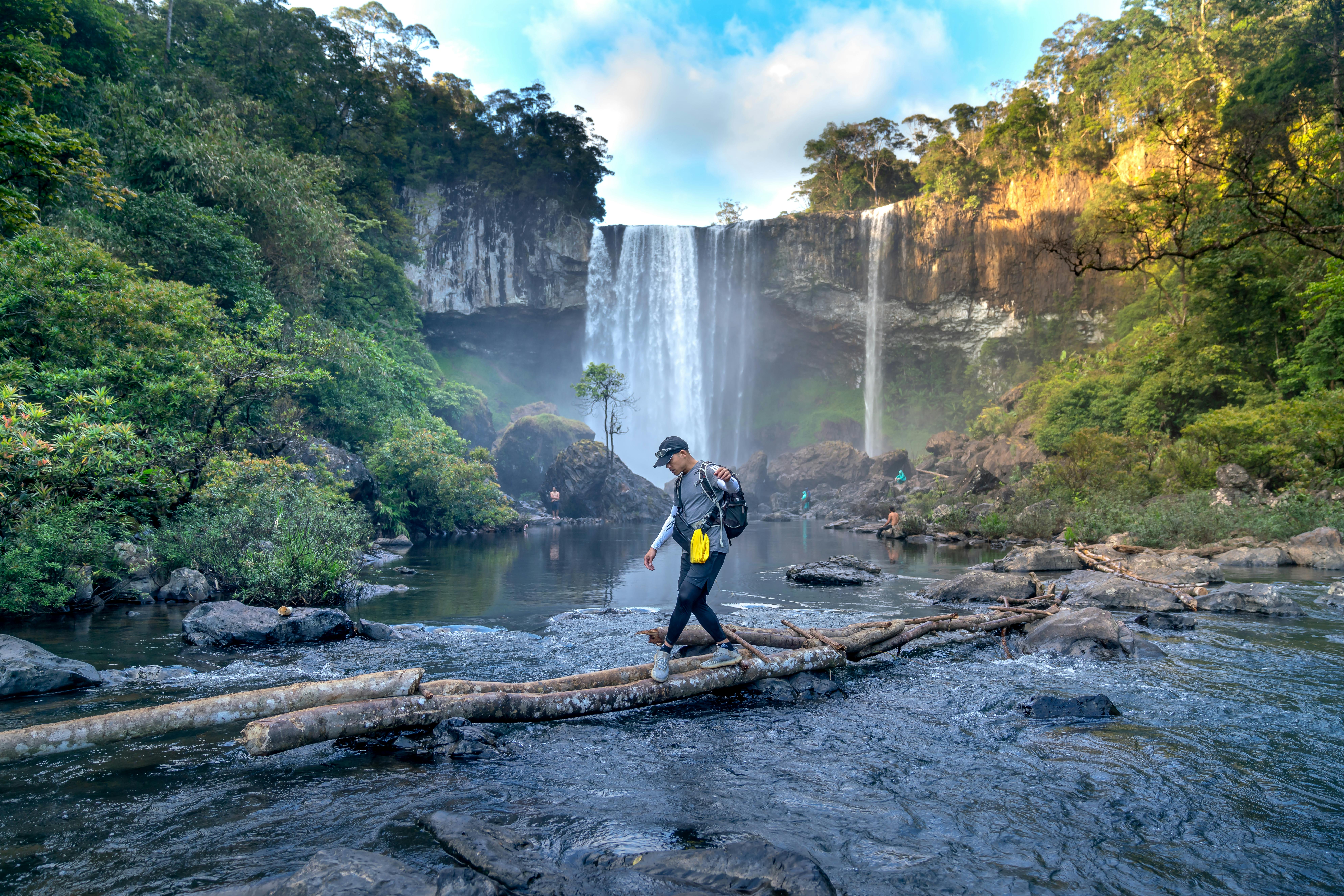 A man walking across a lake with a waterfall in the back being adventurous